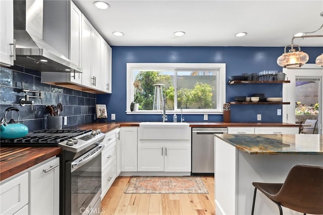 23906 Fernmead Ln, Harbor City, CA 90710 - kitchen with wall chimney range hood, appliances with stainless steel finishes, butcher block counters, light wood-style flooring, and white cabinets