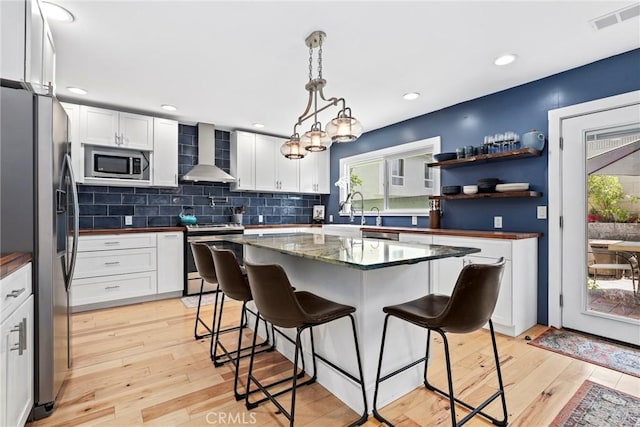 23906 Fernmead Ln, Harbor City, CA 90710 - kitchen featuring appliances with stainless steel finishes, wall chimney exhaust hood, a kitchen breakfast bar, light wood finished floors, and white cabinets