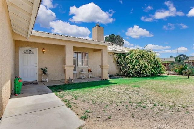 21919 Standing Rock Ave, Apple Valley, CA 92307 - doorway to property featuring a chimney, stucco siding, a yard, and a patio