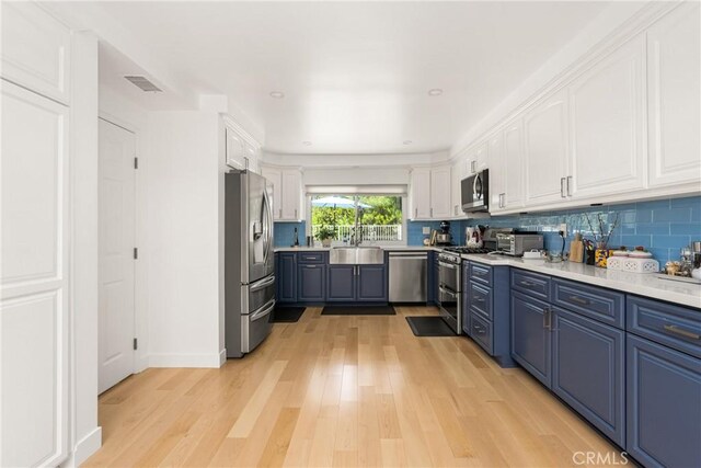 8009 E Eucalyptus Trl, Orange, CA 92869 - kitchen featuring stainless steel appliances, white cabinetry, light wood finished floors, blue cabinetry, and tasteful backsplash