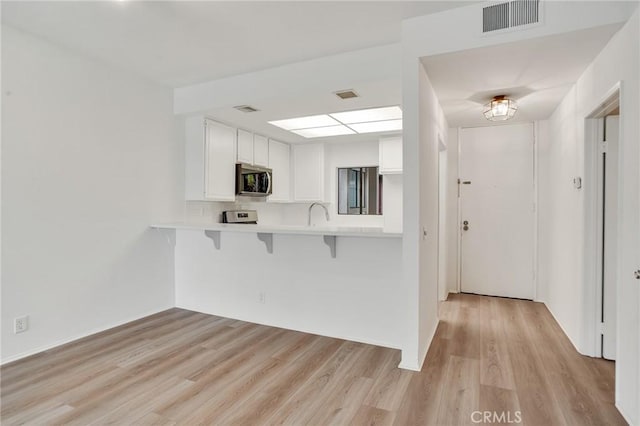 3480 Barham Blvd Unit 215, Los Angeles, CA 90068 - kitchen with stainless steel microwave, a kitchen breakfast bar, light wood-style floors, light countertops, and white cabinets