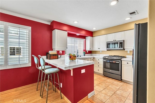 565 N Pageant Dr Unit B, Orange, CA 92869 - kitchen with stainless steel appliances, a peninsula, white cabinets, a breakfast bar area, and ornamental molding