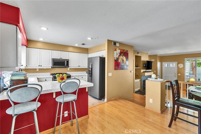 565 N Pageant Dr Unit B, Orange, CA 92869 - kitchen with stainless steel appliances, a peninsula, tile counters, white cabinetry, and light wood-type flooring
