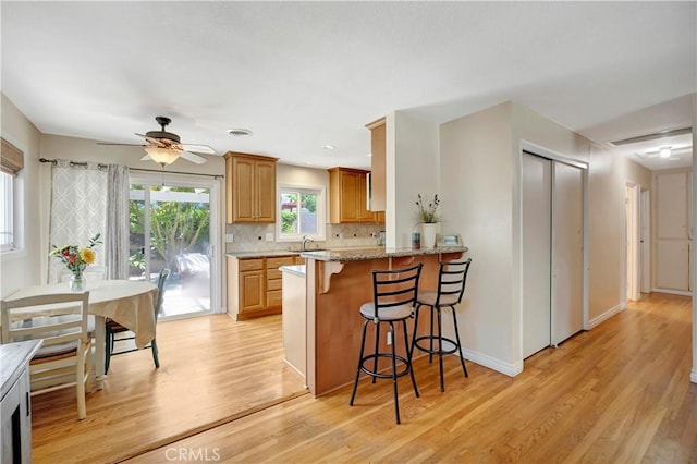 15041 Columbia Ln, Huntington Beach, CA 92647 - kitchen featuring a kitchen bar, light wood finished floors, tasteful backsplash, light stone counters, and a ceiling fan