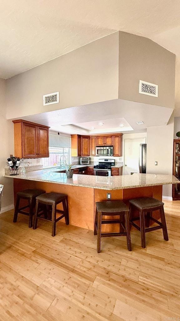 14330 Jennings Vista Way, Lakeside, CA 92040 - kitchen with appliances with stainless steel finishes, brown cabinetry, a breakfast bar, light wood-type flooring, and a towering ceiling