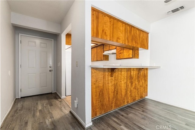 10710 El Camino Real Unit 14, Atascadero, CA 93422 - kitchen featuring brown cabinets, under cabinet range hood, dark wood-style flooring, a breakfast bar, and light countertops