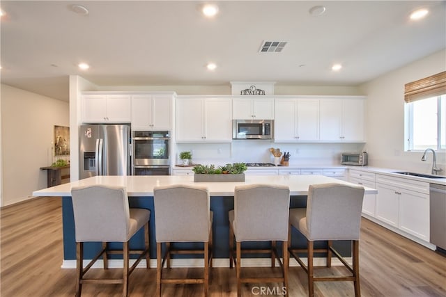 33084 Toledo Bend Ct, Winchester, CA 92596 - kitchen with stainless steel appliances, a kitchen island, wood finished floors, white cabinetry, and recessed lighting