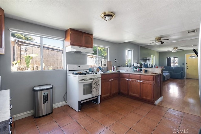 11001 Duncan Ave, Lynwood, CA 90262 - kitchen with white gas stove, under cabinet range hood, a peninsula, ceiling fan, and open floor plan