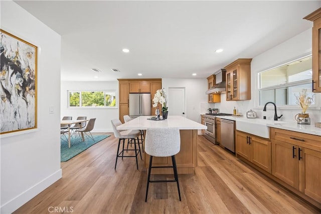 1809 Celeste Ln, Fullerton, CA 92833 - kitchen featuring appliances with stainless steel finishes, wall chimney range hood, a breakfast bar, light wood-type flooring, and brown cabinets