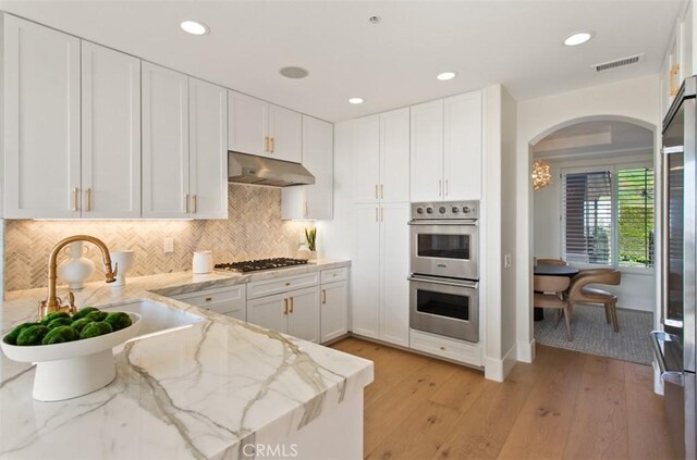 7 Suprema Dr, Newport Coast, CA 92657 - kitchen with stainless steel appliances, under cabinet range hood, arched walkways, white cabinets, and recessed lighting