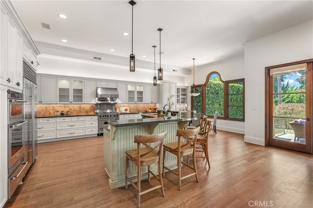 1337 8th St, Manhattan Beach, CA 90266 - kitchen with dark countertops, backsplash, stainless steel stove, under cabinet range hood, and glass insert cabinets