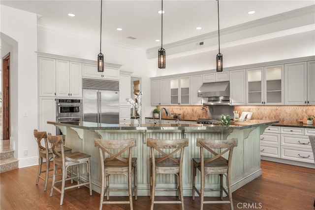 1337 8th St, Manhattan Beach, CA 90266 - kitchen with appliances with stainless steel finishes, under cabinet range hood, backsplash, crown molding, and glass insert cabinets