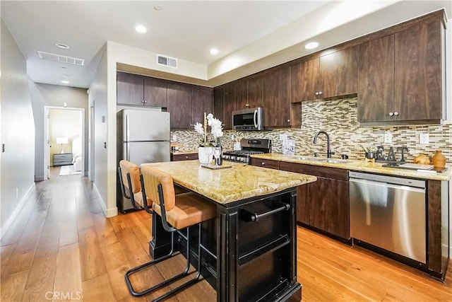1002 Leighton Ave, Los Angeles, CA 90037 - kitchen featuring appliances with stainless steel finishes, decorative backsplash, dark brown cabinets, a breakfast bar area, and a center island