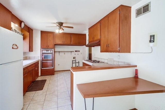 1970 El Prado Ave, Lemon Grove, CA 91945 - kitchen featuring freestanding refrigerator, a ceiling fan, a peninsula, brown cabinetry, and double oven