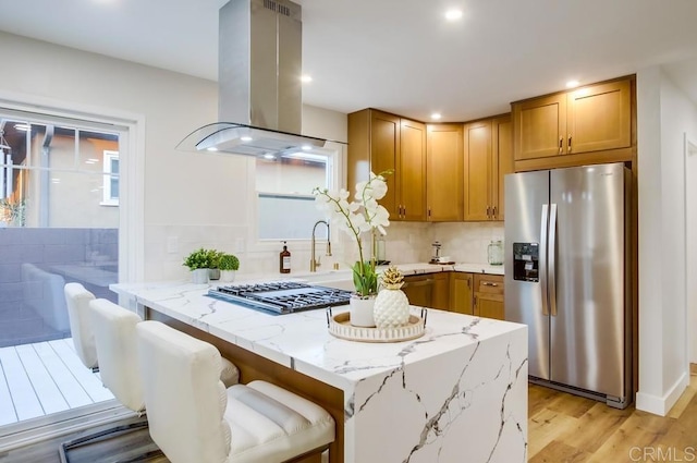 482 Wykes St, Chula Vista, CA 91911 - kitchen with appliances with stainless steel finishes, island exhaust hood, light stone counters, light wood-type flooring, and tasteful backsplash