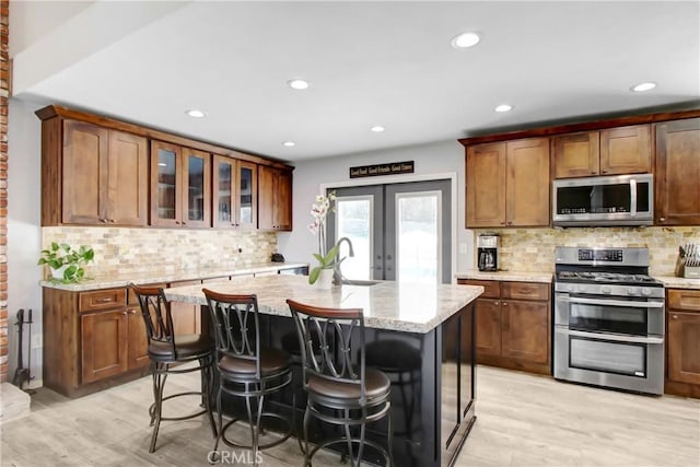17321 Sunset View Dr, Riverside, CA 92504 - kitchen featuring appliances with stainless steel finishes, decorative backsplash, light wood finished floors, a kitchen island with sink, and recessed lighting