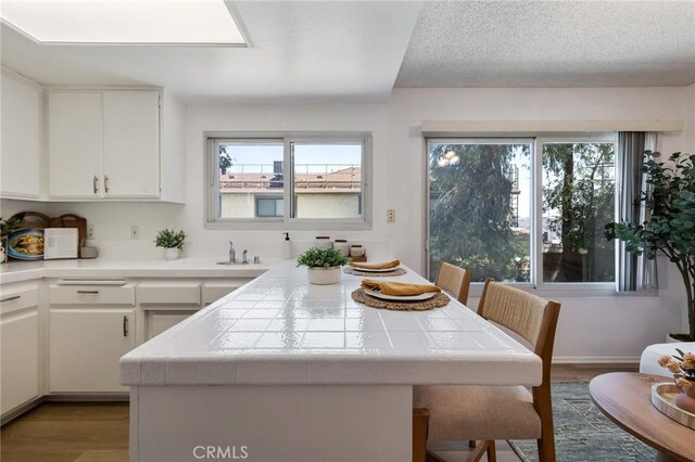 7038 De Celis Pl Unit 4, Van Nuys, CA 91406 - kitchen with tile countertops, light wood-type flooring, white cabinets, and a kitchen breakfast bar