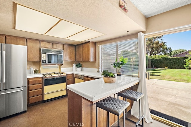 11551 Gladstone Cir, Fountain Valley, CA 92708 - kitchen with stainless steel appliances, brown cabinets, a peninsula, tile countertops, and a kitchen bar