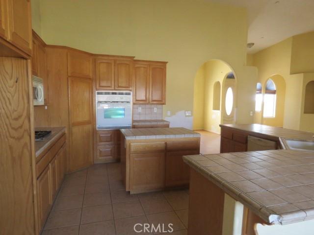 2425 Tokay Rd, Phelan, CA 92371 - kitchen featuring white appliances, tile counters, a kitchen island, a high ceiling, and light tile patterned flooring