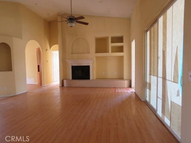 2425 Tokay Rd, Phelan, CA 92371 - unfurnished living room with built in shelves, light wood-type flooring, high vaulted ceiling, arched walkways, and ceiling fan