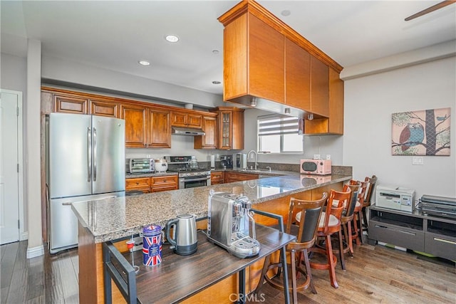 1026 S Oxford Ave Unit 206, Los Angeles, CA 90006 - kitchen featuring appliances with stainless steel finishes, under cabinet range hood, brown cabinets, stone countertops, and recessed lighting