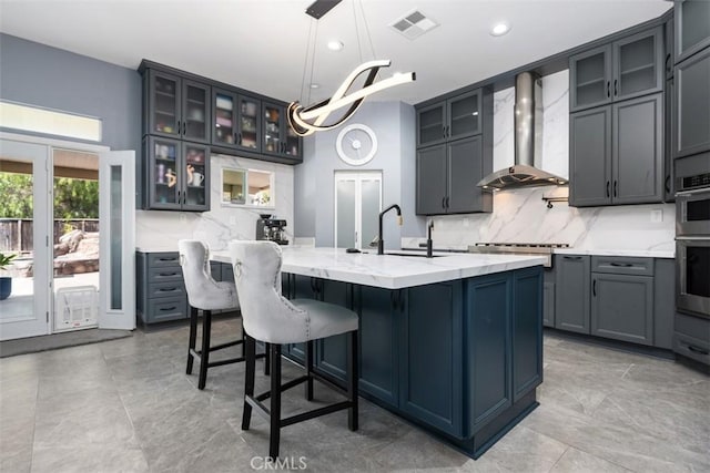 185 Alabaster Loop, Perris, CA 92570 - kitchen featuring wall chimney range hood, an island with sink, decorative backsplash, recessed lighting, and light stone countertops