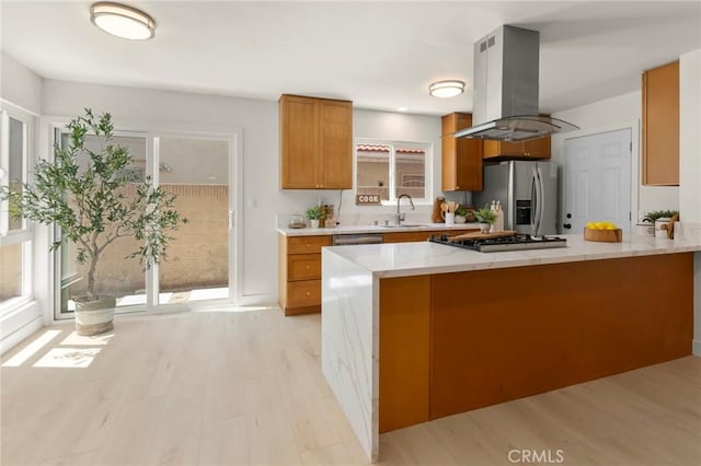 17698 Locust St, Fountain Valley, CA 92708 - kitchen featuring island range hood, stainless steel appliances, brown cabinets, a peninsula, and light wood finished floors
