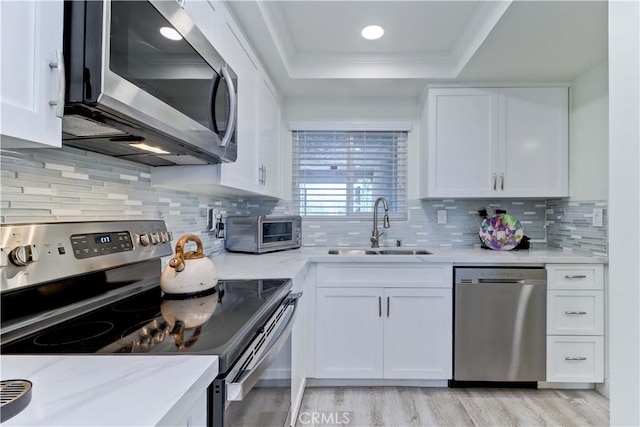 3365 Punta Alta Unit 2F, Laguna Woods, CA 92637 - kitchen featuring appliances with stainless steel finishes, a tray ceiling, white cabinetry, light wood-style floors, and ornamental molding