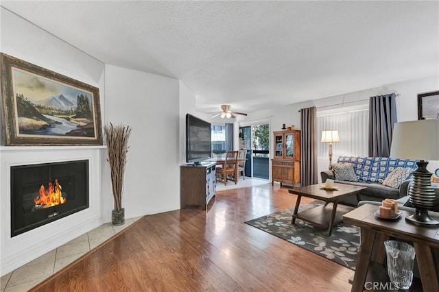 26966 Flo Ln Unit 319, Canyon Country, CA 91351 - living room featuring wood finished floors, a ceiling fan, a warm lit fireplace, and a textured ceiling
