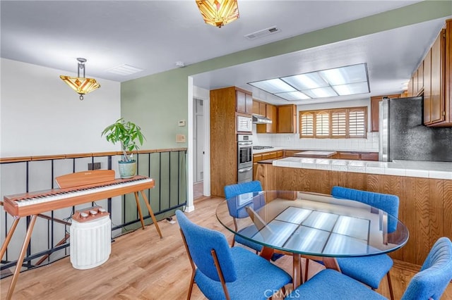 2433 S Gaffey St, San Pedro, CA 90731 - kitchen featuring stainless steel appliances, tile countertops, brown cabinets, light wood-style flooring, and tasteful backsplash