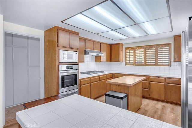 2433 S Gaffey St, San Pedro, CA 90731 - kitchen with stainless steel appliances, under cabinet range hood, tasteful backsplash, light wood-style flooring, and brown cabinets