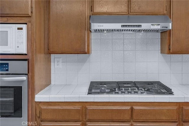 2433 S Gaffey St, San Pedro, CA 90731 - kitchen with exhaust hood, stainless steel appliances, tile countertops, backsplash, and brown cabinetry