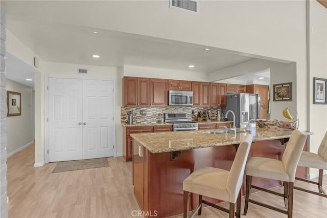 12674 Metate Ln, Poway, CA 92064 - kitchen featuring appliances with stainless steel finishes, a kitchen bar, brown cabinetry, light wood-type flooring, and tasteful backsplash