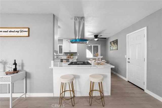 11343 1st Ave, Hesperia, CA 92345 - kitchen with white cabinetry, a peninsula, a ceiling fan, a breakfast bar area, and island range hood