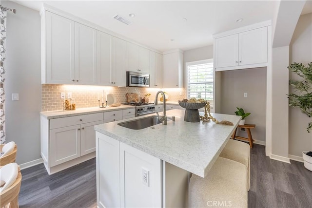 134 Milky Way, Irvine, CA 92618 - kitchen with stainless steel microwave, dark wood finished floors, tasteful backsplash, an island with sink, and white cabinetry
