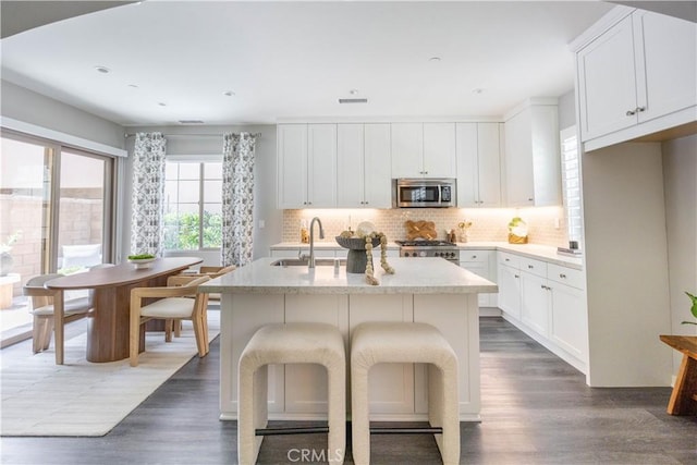 134 Milky Way, Irvine, CA 92618 - kitchen featuring appliances with stainless steel finishes, dark wood-type flooring, decorative backsplash, an island with sink, and light stone countertops