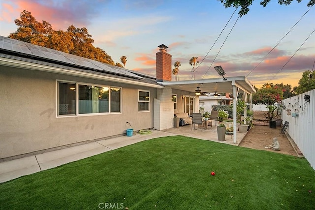 7985 Stella St, Riverside, CA 92504 - back of property at dusk featuring a fenced backyard, ceiling fan, solar panels, a patio area, and a chimney