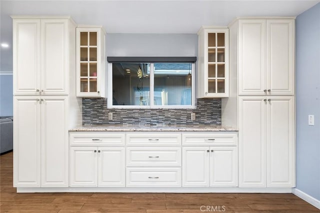 7985 Stella St, Riverside, CA 92504 - kitchen with tasteful backsplash, glass insert cabinets, light stone counters, and wood finished floors