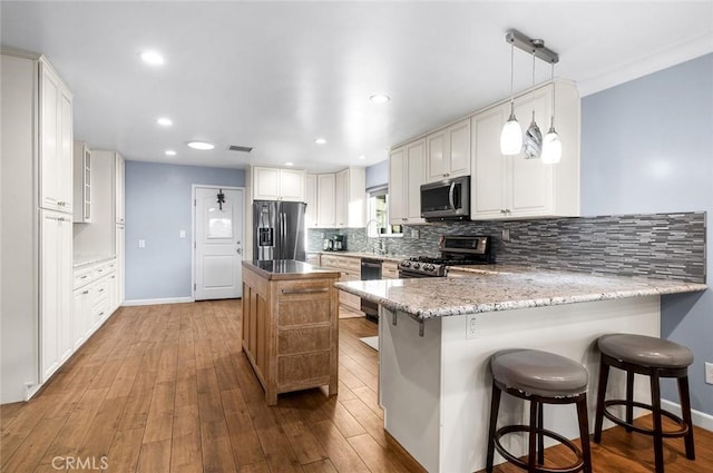 7985 Stella St, Riverside, CA 92504 - kitchen with appliances with stainless steel finishes, decorative backsplash, a peninsula, wood finished floors, and a center island