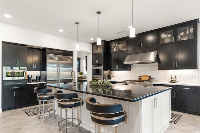 41783 Valencia Way, Temecula, CA 92592 - kitchen featuring range hood, appliances with stainless steel finishes, tasteful backsplash, a center island with sink, and glass insert cabinets