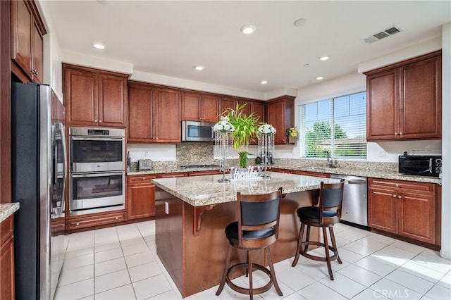 13243 Stanton Dr, Rancho Cucamonga, CA 91739 - kitchen with appliances with stainless steel finishes, a center island with sink, light tile patterned flooring, a breakfast bar area, and light stone countertops