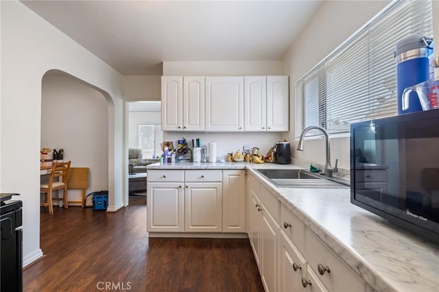 228 S 4th St, Santa Paula, CA 93060 - kitchen with white cabinetry, dark wood-type flooring, black microwave, arched walkways, and light stone countertops