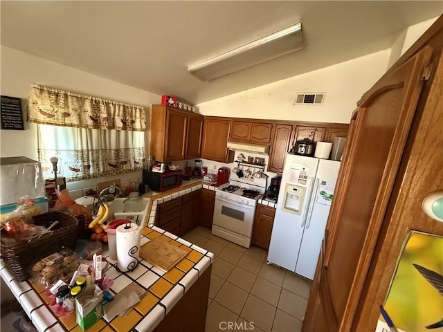 5320 Jonah St, Bakersfield, CA 93307 - kitchen with white appliances, tile counters, vaulted ceiling, light tile patterned flooring, and brown cabinetry