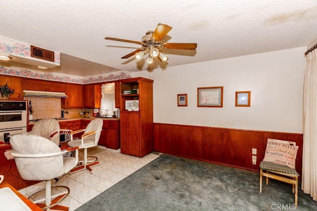 17480 Fontlee Ln, Fontana, CA 92335 - kitchen with under cabinet range hood, a ceiling fan, a textured ceiling, wainscoting, and wooden walls
