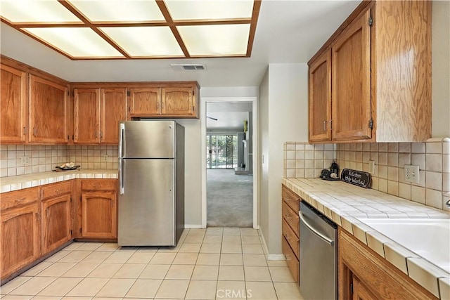 524 St Kevin Ct, Merced, CA 95348 - kitchen featuring stainless steel appliances, tile countertops, light tile patterned floors, decorative backsplash, and brown cabinets