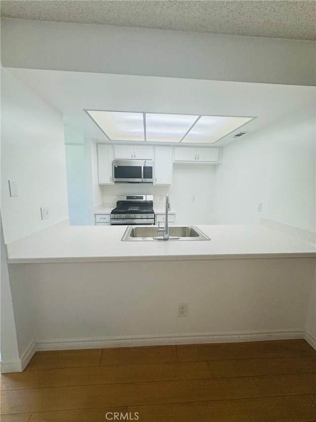 5484 Dobbs St Unit 132, Los Angeles, CA 90032 - kitchen featuring stainless steel appliances, a peninsula, white cabinetry, wood finished floors, and light countertops