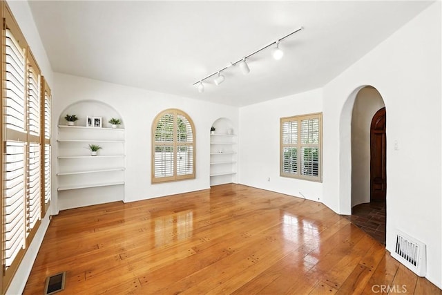 408 N Mccadden Pl, Los Angeles, CA 90004 - unfurnished living room featuring built in shelves, hardwood / wood-style floors, arched walkways, and track lighting