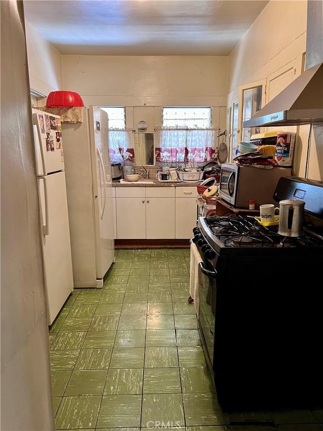 1323 W 41st Pl, Los Angeles, CA 90037 - kitchen with black range with gas stovetop, freestanding refrigerator, white cabinetry, tile patterned floors, and exhaust hood