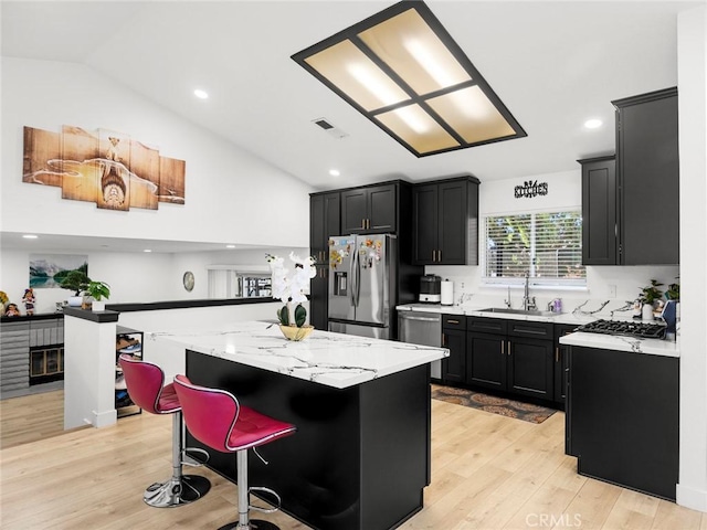 1324 Windermere Ct, Palmdale, CA 93551 - kitchen featuring appliances with stainless steel finishes, dark cabinetry, lofted ceiling, a center island, and light wood finished floors