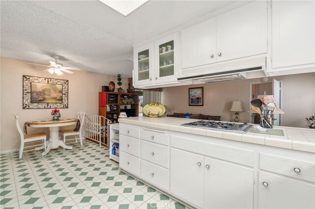 17655 Vine Ct, Fontana, CA 92335 - kitchen featuring stainless steel gas cooktop, under cabinet range hood, tile counters, white cabinetry, and ceiling fan
